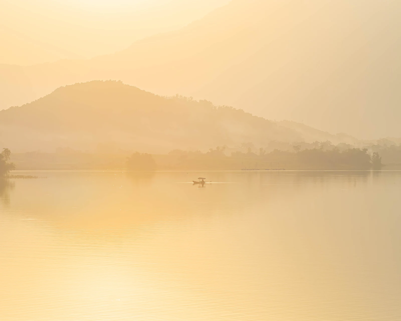 A small boat crossing a still lake in golden morning mist, hills behind